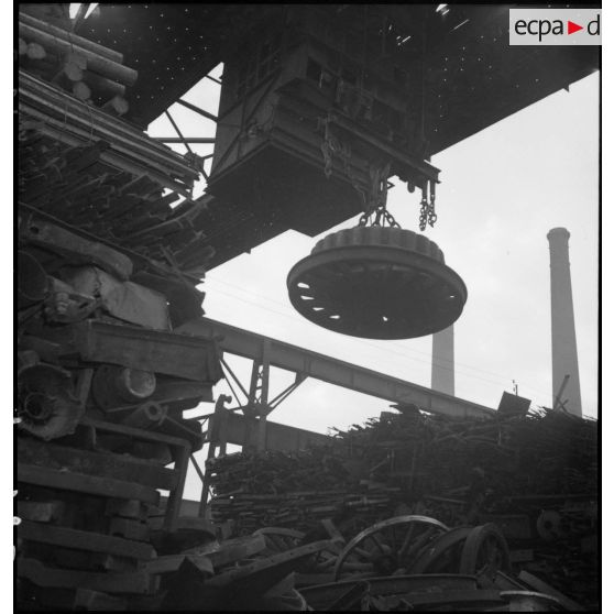 Un électro-aimant supporté par une grue portique est photographié en plan général en contre-plongée.