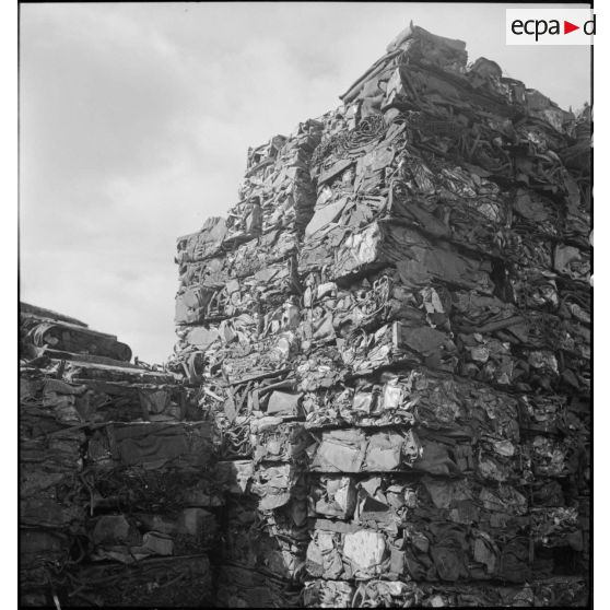 Des blocs de ferraille compressée sont photographiés en plan général à l'extérieur de l'usine.