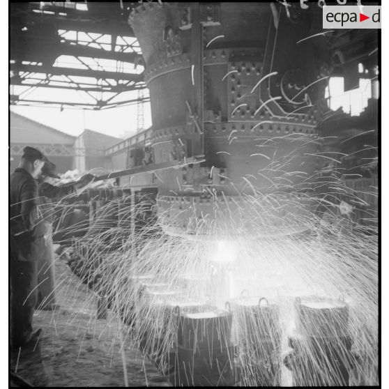 A l'intérieur de l'usine des ouvriers travaillent devant un fourneau.