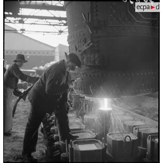 A l'intérieur de l'usine des ouvriers travaillent devant un fourneau.
