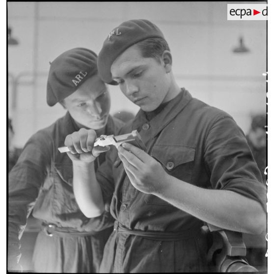 Plan américain de deux élèves qui mesurent une pièce métallique avec un pied à coulisse.