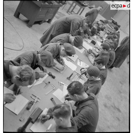 Plan général d'élèves apprentis, qui assis à une table, étudient en atelier.