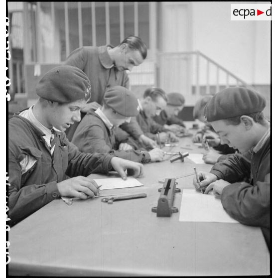 Plan général d'élèves apprentis, qui assis à une table, étudient en atelier.
