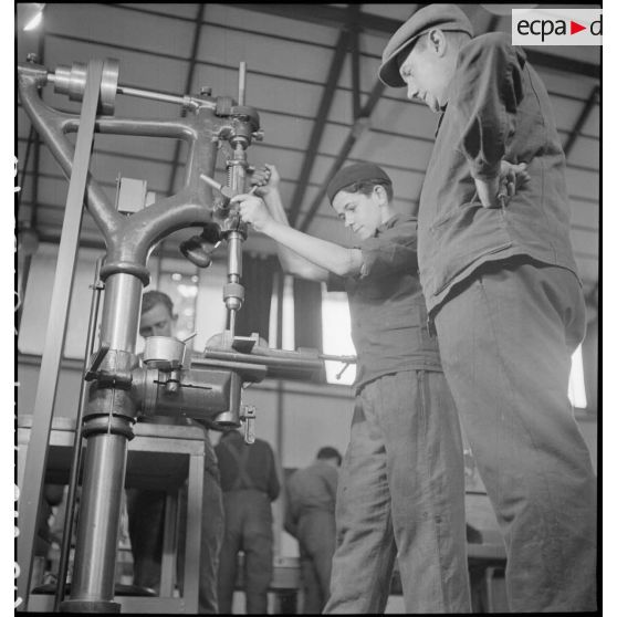 En atelier un professeur assiste un élève apprenti qui travaille sur une machine-outil.