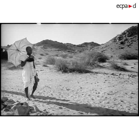 Un pèlerin en tenue d'irham marche dans le désert en tenant une ombrelle.