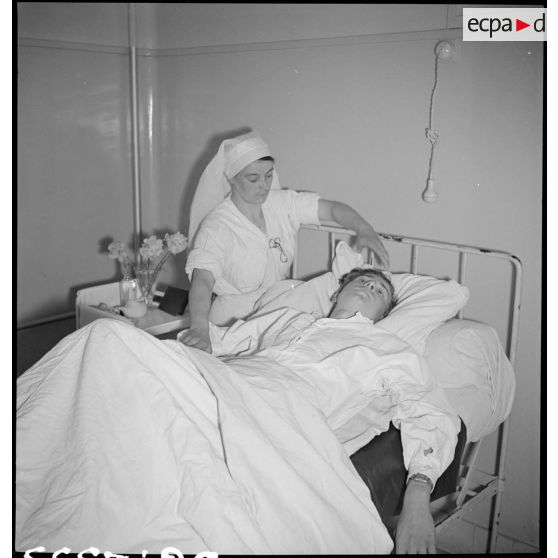 Dans un hôpital une infirmière soigne un blessé alité, victime civile d'un bombardement allemand.