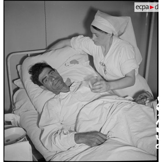 Dans un hôpital une infirmière soigne un blessé alité, victime civile d'un bombardement allemand.