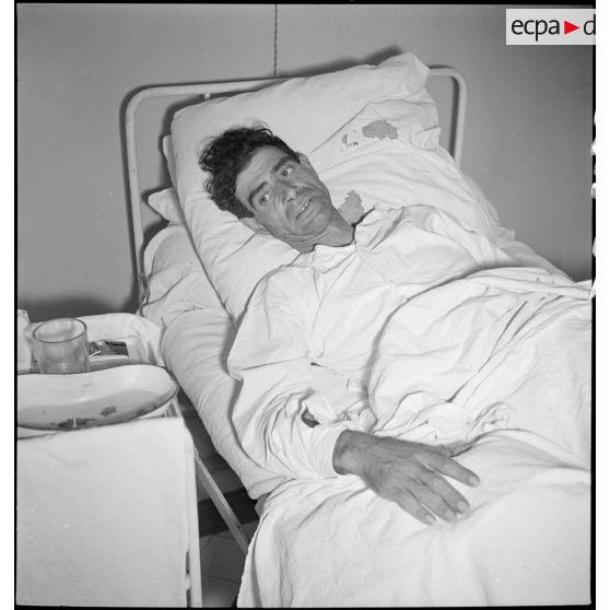 Dans un hôpital plan moyen d'un blessé alité, victime civile d'un bombardement allemand.