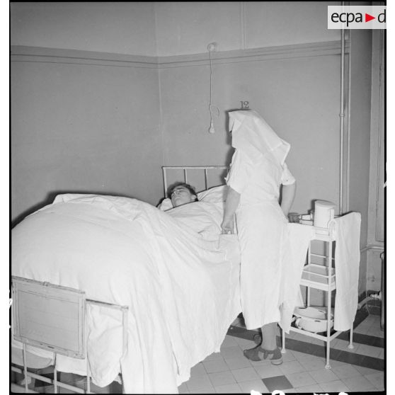 Dans un hôpital une infirmière soigne un blessé alité, victime civile d'un bombardement allemand.