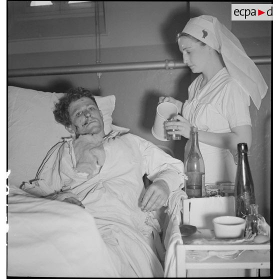 Dans un hôpital une infirmière soigne un blessé alité, victime civile d'un bombardement allemand.