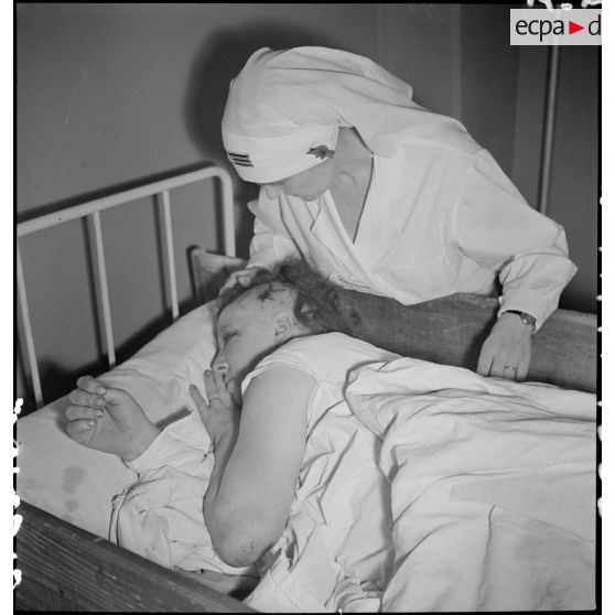 Dans un hôpital une infirmière soigne un blessé alité, victime civile d'un bombardement allemand.
