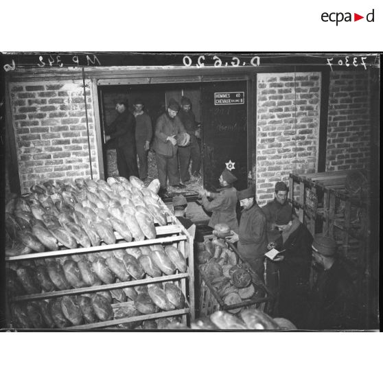Des soldats rangent des boules de pains dans de vastes paniers métalliques.