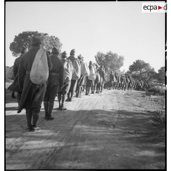 Des soldats des troupes coloniales marchent en colonne sur une route.