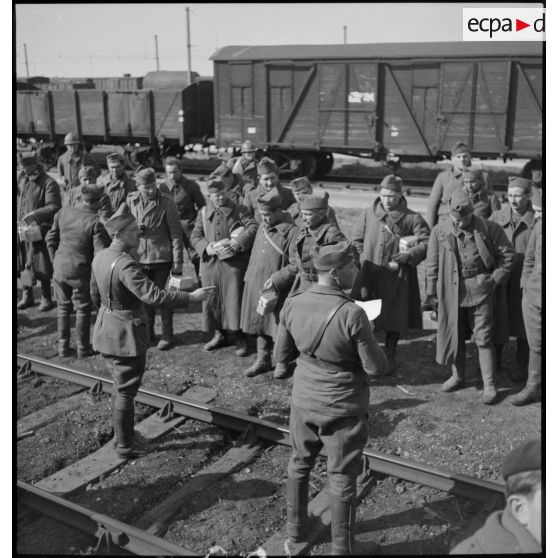 Des soldats se rassemblent près d'une voie ferrée gamelles en main.