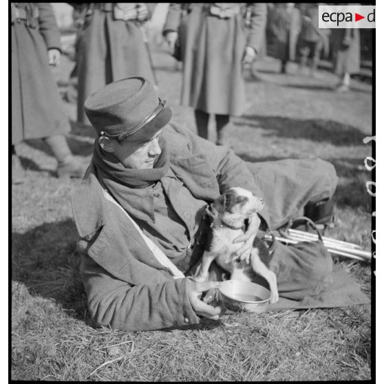 Plan moyen d'un soldat couché au sol avec un petit chien dans les bras.