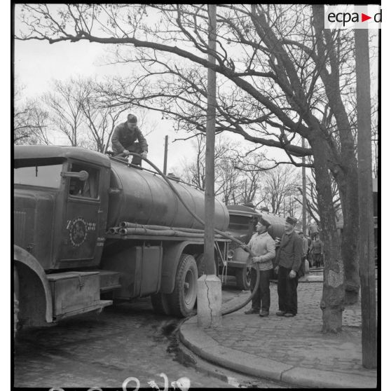 Des soldats vidangent un camion-citerne transportant du vin. La scène est photographiée en plan général. Le camion-citerne appartient au 19e escadron du train de Paris.