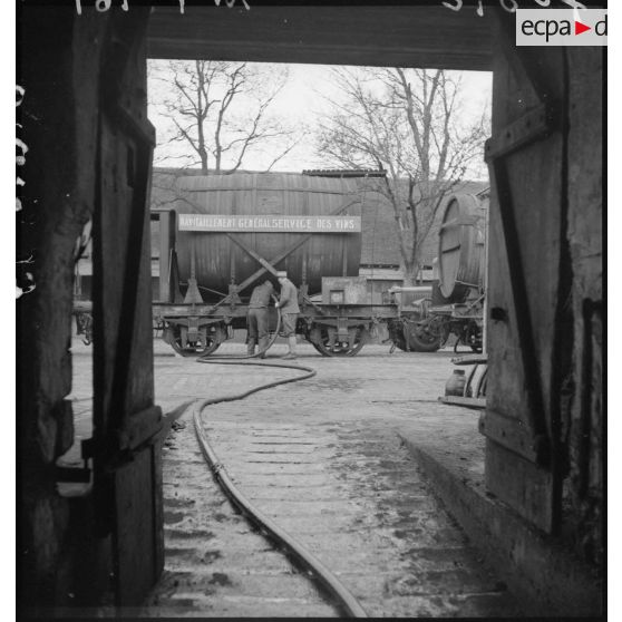 Des soldats vidangent un wagon-citerne transportant du vin. La scène est photographiée en plan général. Le camion-citerne appartient au 19e escadron du train de Paris.