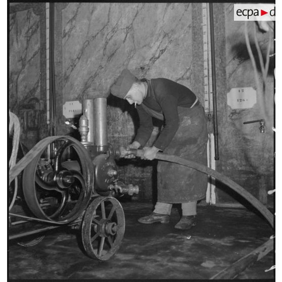 Dans une pièce, un soldat branche un tuyau sur une pompe.
