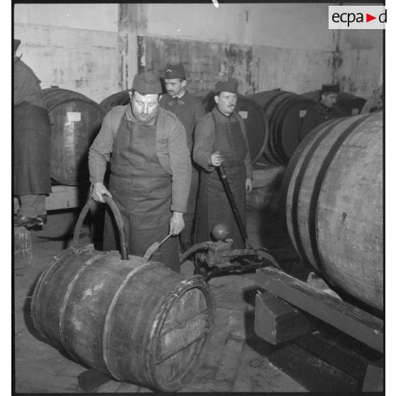 Dans une pièce, des soldats remplissent des tonneaux de vins.