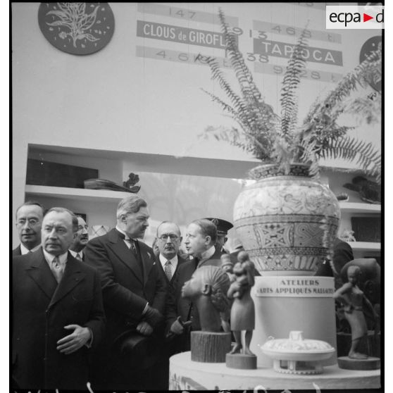 Lors de l'inauguration, Monsieur Georges Mandel, ministre des colonies, se tient devant un stand de l'exposition la France d'outremer en compagnie d'autres personnalités civiles.