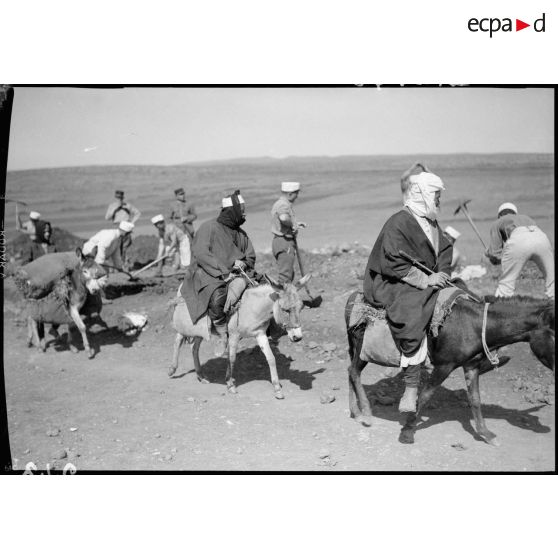 Deux bédouins sur des ânes passent sur la route alors que les légionnaires du 6e REI travaillent à sa construction.