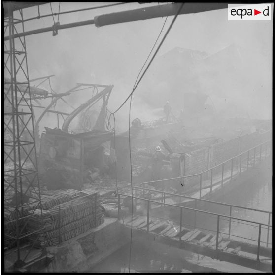 Des pompiers éteignent l'incendie d'un hangar détruit par le bombardement aérien allemand.