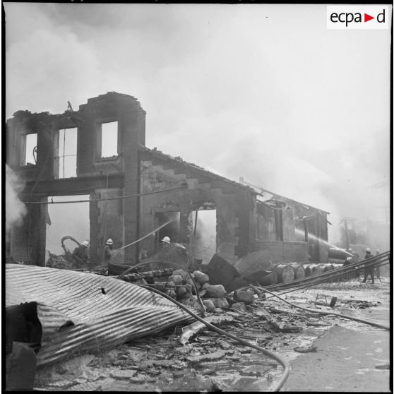 Des pompiers éteignent l'incendie d'un hangar détruit par le bombardement aérien allemand.