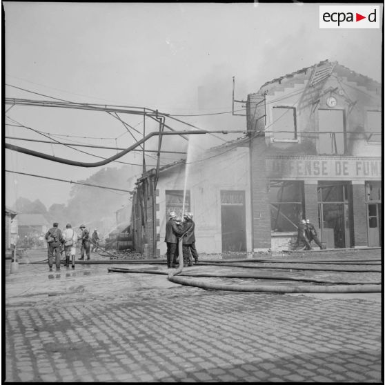 Des pompiers éteignent l'incendie d'un hangar détruit par le bombardement aérien allemand.