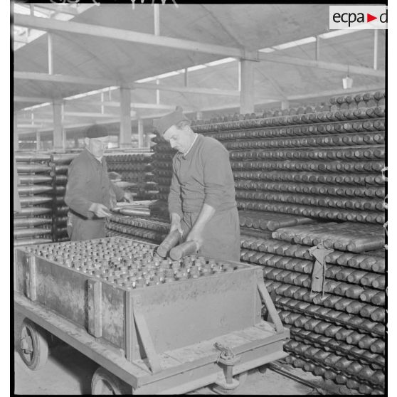 Des ouvriers rangent des obus dans des caisses de bois.