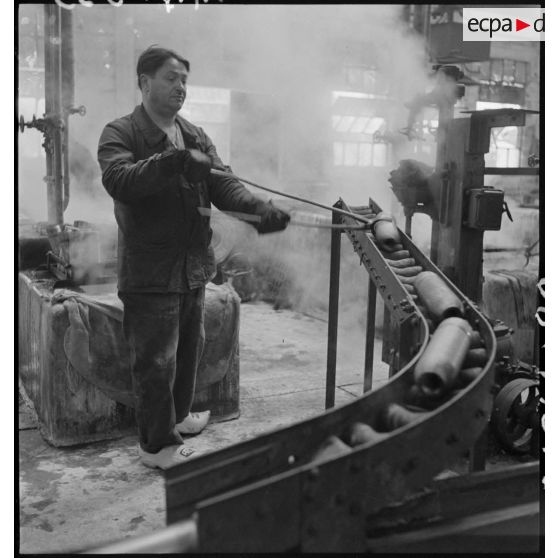 Un ouvrier se sert d'une pince pour saisir un corps d'obus.