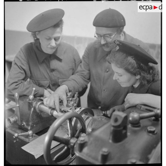 Un professeur assiste deux élèves féminines qui travaillent sur une machine-outil en atelier.