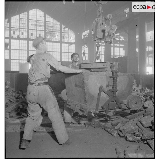 Des ouvriers manipulent un caisson métallique.