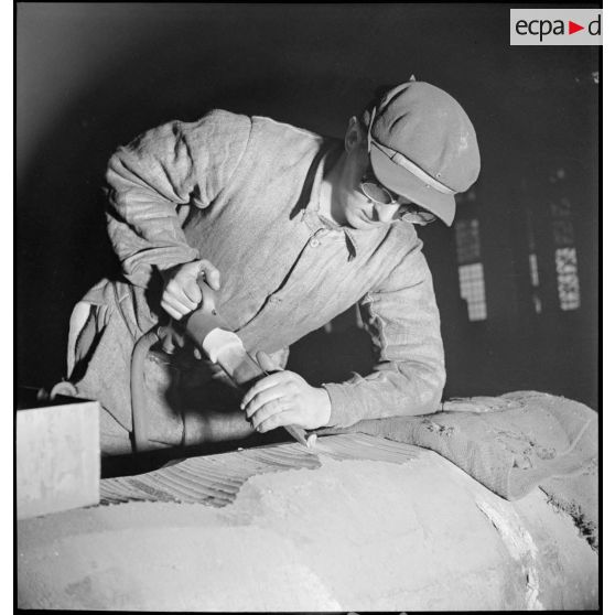 Un ouvrier travaille avec un burin pneumatique sur un corps métallique.