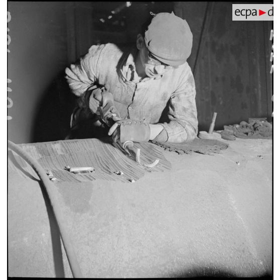 Un ouvrier travaille avec un burin pneumatique sur un corps métallique.