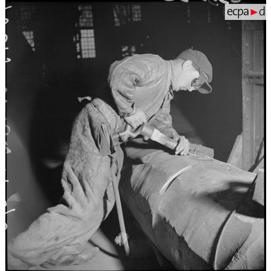 Un ouvrier travaille avec un burin pneumatique sur un corps métallique.