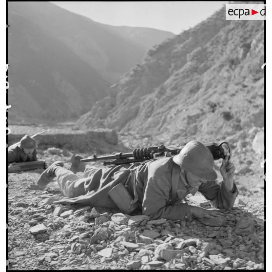 Plan moyen d'un tirailleur du 1er RTA qui rampe avec une mitrailleuse de 8 mm modèle 1914 Hotchkiss sur le dos.