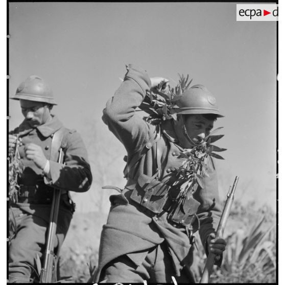 Plan américain de deux tirailleurs du 1er RTA qui se camouflent avec de la végétation.