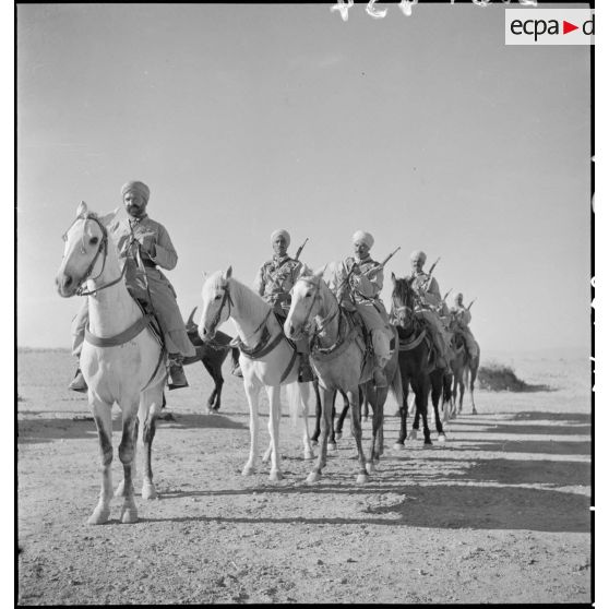 Une colonne de spahis algériens à cheval est photographiée à l'arrêt en contre-plongée dans le désert.