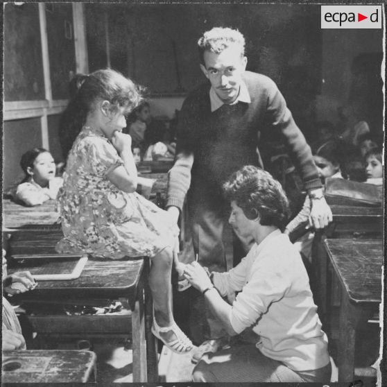 Mouvement de solidarité féminine (MSF) en Algérie. Cercle féminin. Une femme attache une chaussure à une enfant dans la classe.