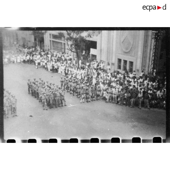 Lors d'une grande réunion, des éléments des troupes coloniales et de la Légion étrangère se tiennent au garde-à-vous, sur la place devant l'Hôtel de Ville de Saigon. [description provisoire]