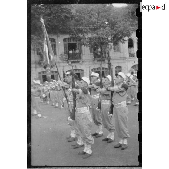 Lors d'une grande réunion, des éléments des troupes coloniales et de la Légion étrangère se tiennent au garde-à-vous, sur la place devant l'Hôtel de Ville de Saigon. [description provisoire]