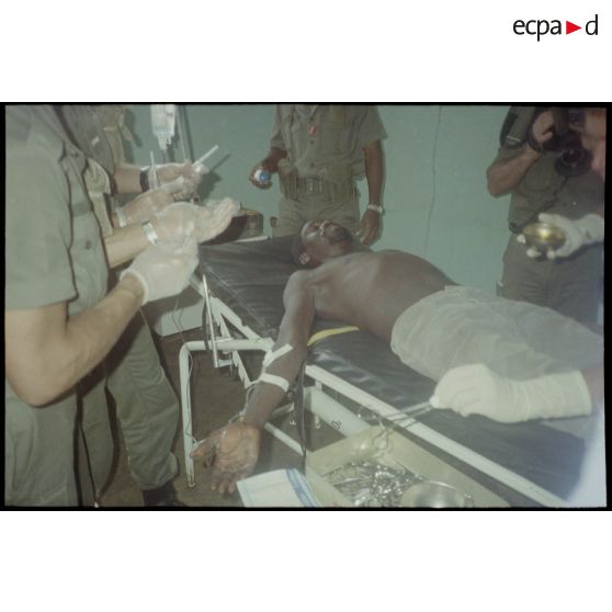 Intervention et opération chirurgicale sur un patient blessé à la main dans un dispensaire à Karama par les membres de l'antenne chirurgicale parachutiste (ACP).