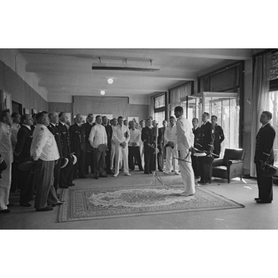 Sur la gauche, en tenue blanche, le capitaine (kapitänleutnant) Herbert Sohler, représentant de la 7.Unterseebootsflottille, prononce un discours lors de l'inauguration d'une exposition de dessins et de photographies.