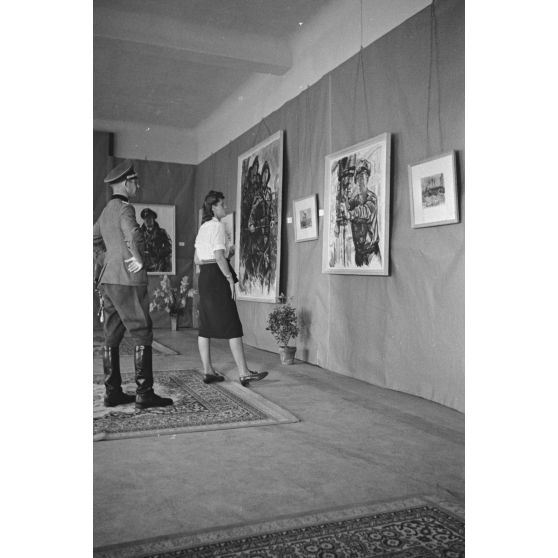 Une femme et un officier de la Wehrmacht visitent l'exposition consacrée aux peintures de Lothar-Günther Buchheim et de Richard Schreiber à l'hôtel Royal de La Baule.