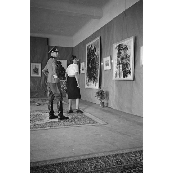 Une femme et un officier de la Wehrmacht visitent l'exposition consacrée aux peintures de Lothar-Günther Buchheim et de Richard Schreiber à l'hôtel Royal de La Baule.