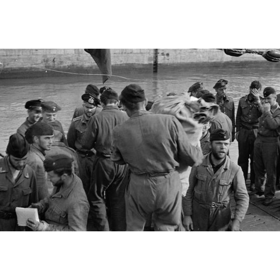 A Saint-Nazaire, sur le pont d'un sous-marin allemand, l'équipage, à peine de retour de mission en mer, commence tout juste à se détendre et à décharger le matériel.