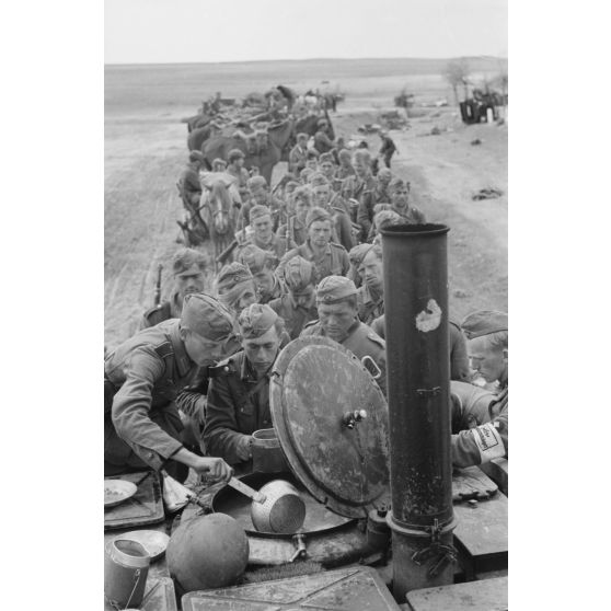 Des fantassins de la 137. infanterie division patientent devant une cuisine roulante.