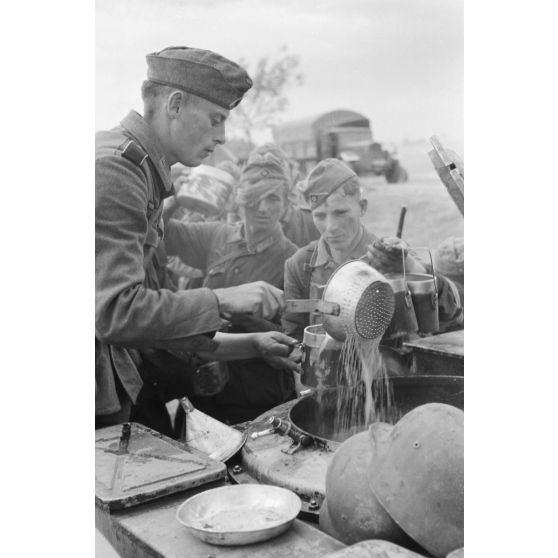 Des fantassins de la 137. infanterie division patientent devant une cuisine roulante.