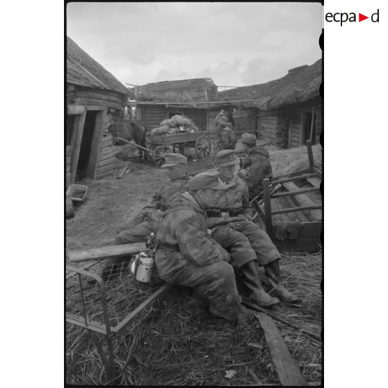 Alors que les Nashorn avancent prudemment, des fantassins patientent entre deux isbas abandonnées.