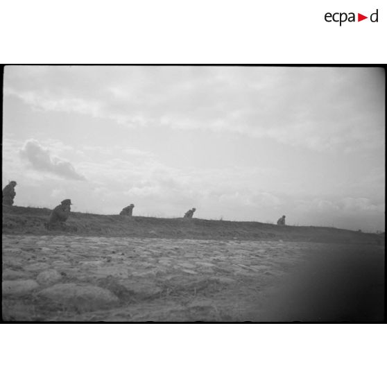 Des fantassins progressent le long d'un talus.